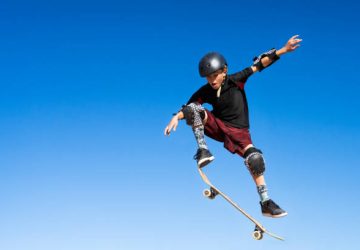 Young Boy on A Skateboard Jumping Into the Air.  Isolated on the blue sky.