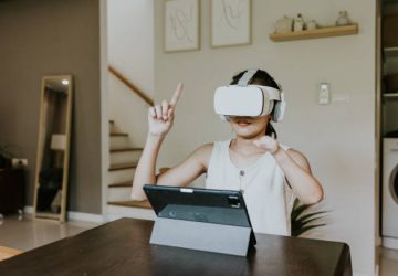 Happy young adult woman enjoy her online class at home, wearing virtual reality simulator and watching display inside.